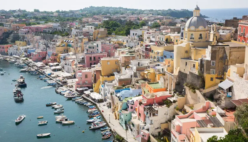 Colorate case a picco sul mare, un porto con barche. La vista ricorda la vicinanza tra Ischia e Capri, un sogno di vacanza.