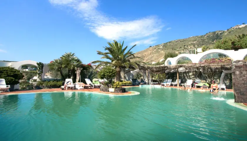 Piscina con palme e lettini, un angolo di paradiso tropicale a Ischia, con persone che si rilassano nell'acqua cristallina.
