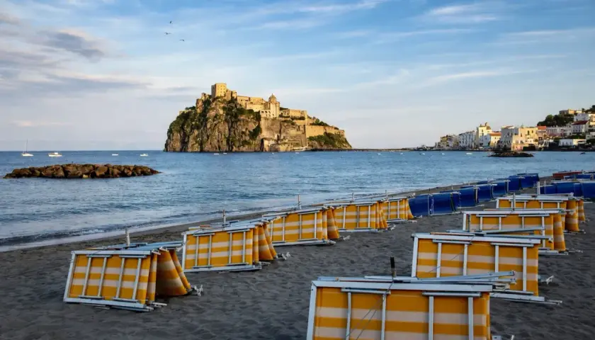 Spiaggia della Mandra a Ischia, con lettini piegati e il Castello Aragonese sullo sfondo.