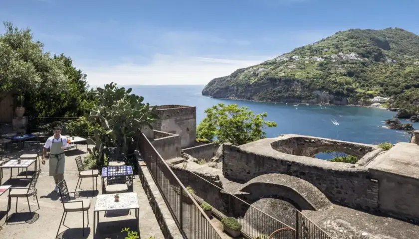 Terrazza con vista mare e un cameriere che serve ai tavoli. Un luogo incantevole, un albergo il monastero con un panorama mozzafiato.