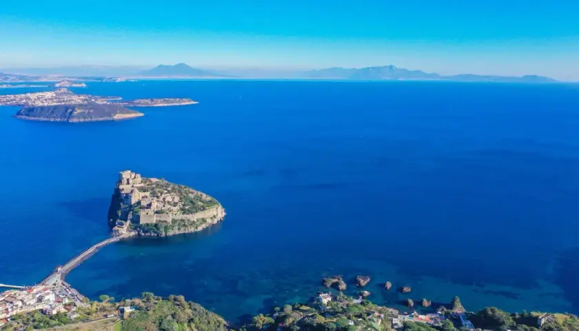 Aerial view of Castello Aragonese on a rocky island connected by a causeway to the coast of Ischia, Italy.
