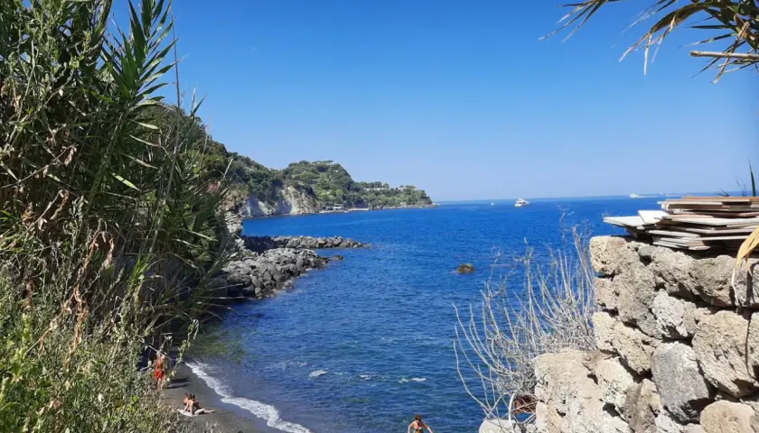 Spiaggia nera con gente che si gode il sole, scogli e il blu intenso del mare degli inglesi.