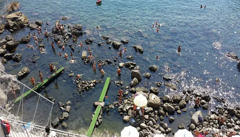 Persone si godono il sole e l'acqua cristallina nelle piscine naturali di Ischia, tra scogli e fondali trasparenti.
