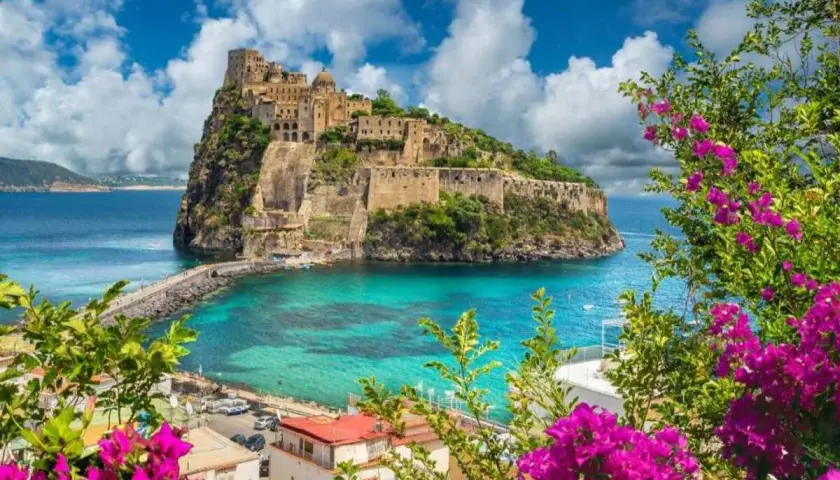 Castello Aragonese su uno scoglio, con mare turchese e fiori viola in primo piano. Una vittoria colonna di bellezza naturale.