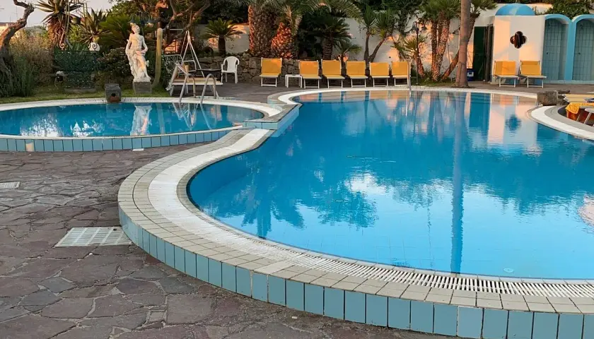 Piscine azzurre e lettini gialli al **hotel Monte Tabor**, un'oasi di relax tra palme e statue.