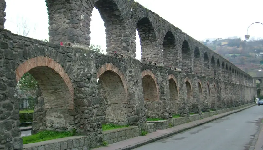 Antichi pilastri in pietra e mattoni, parte di un acquedotto a Ischia, si estendono lungo una strada.
