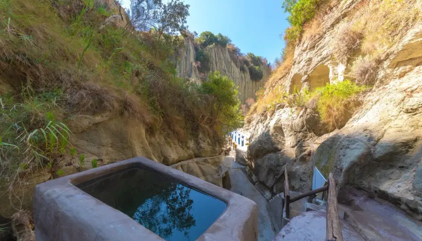 Piscina naturale scavata nella roccia, parte delle storiche terme di Cavascura, circondata da vegetazione e pareti rocciose.