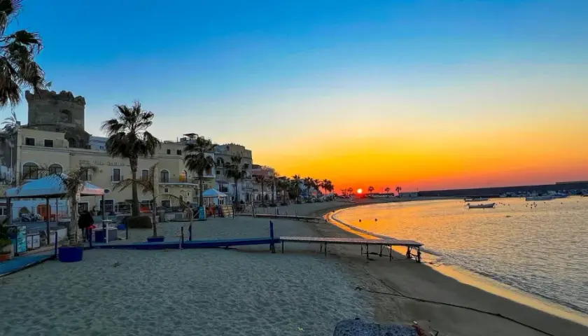 Tramonto dorato sul lungomare di Forio, Ischia. Palme, edifici storici e barche nel porto creano uno scenario incantevole.