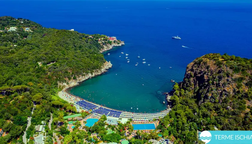 Vista aerea di una baia con spiaggia, mare blu e le piscine Negombo immerse nel verde.