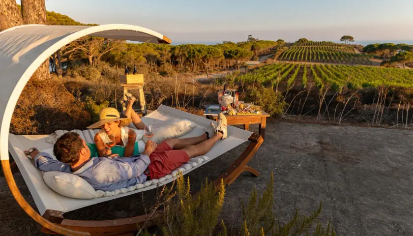 Coppia rilassata su un'amaca con vista su vigneti e mare, sorseggiando vino. Un perfetto sorgeto Ischia aperitivo al tramonto.