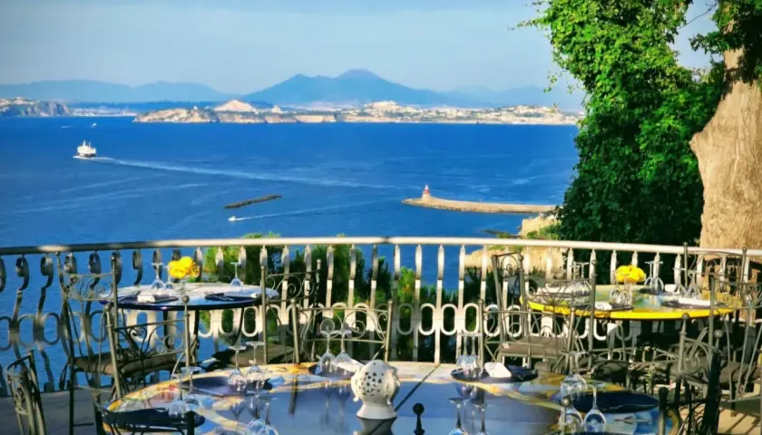 Tavoli apparecchiati con vista mare, un invito a cenare in uno dei ristoranti di Casamicciola. Il Vesuvio sullo sfondo.