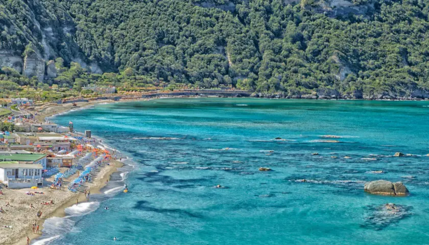 La spiaggia di Citara, con le sue acque cristalline e la rigogliosa vegetazione alle spalle, accoglie bagnanti e ombrelloni colorati.
