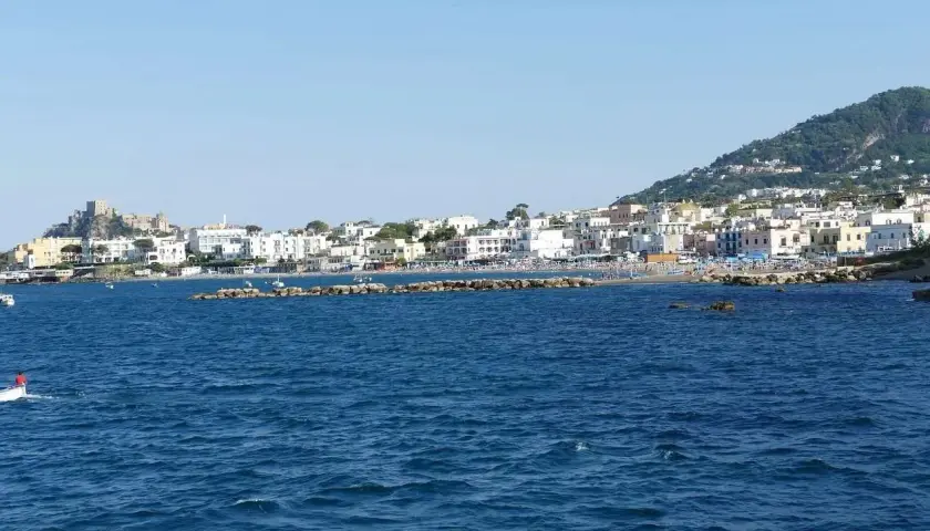 La costa di Ischia vista dal mare, con il castello Aragonese in lontananza. Immagina i traghetti Formia Ischia che ti portano qui.