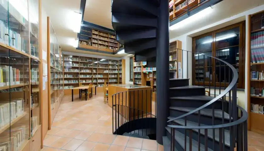 Interno della biblioteca antoniana ischia con scaffali pieni di libri, tavoli e una scala a chiocciola nera.