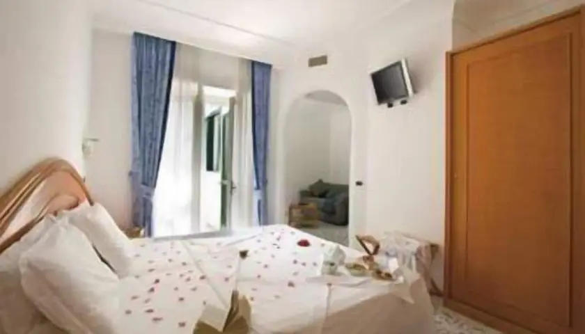 Camera accogliente con letto decorato con petali di rosa, un tavolino con colazione e un armadio in legno. Un'oasi di relax al hotel terme mediterraneo Ischia.