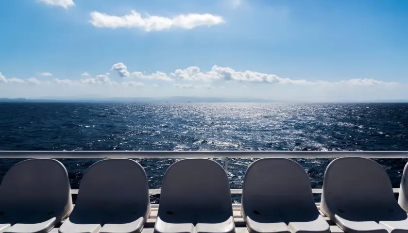 Sedili vuoti su un traghetto, con il mare blu scintillante e le montagne all'orizzonte. La differenza tra aliscafo e traghetto è evidente nella velocità e nel comfort.