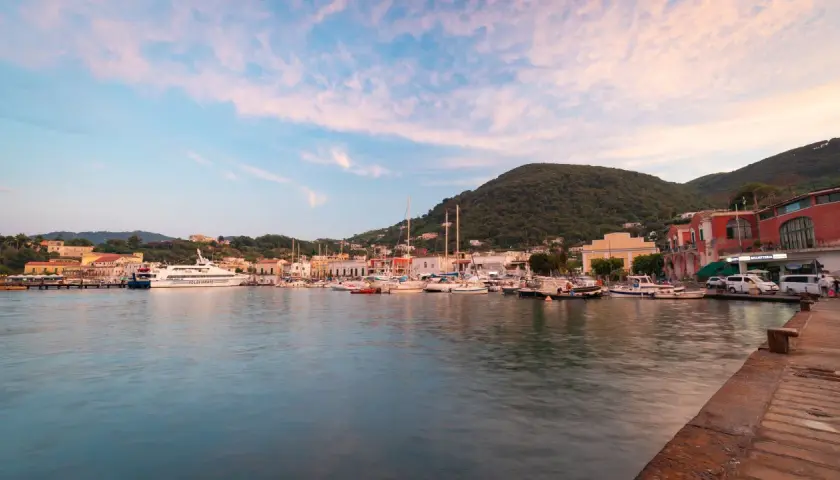 I **porti di Ischia** al tramonto, con barche ormeggiate e colline verdi sullo sfondo.