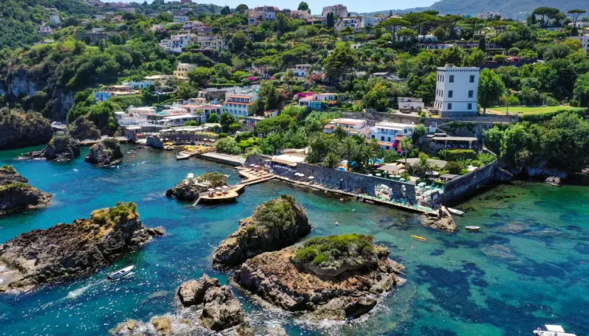Baia di Cartaromana con rocce e acque cristalline. Case arroccate sulla collina. Scopri come arrivare a questa incantevole spiaggia.