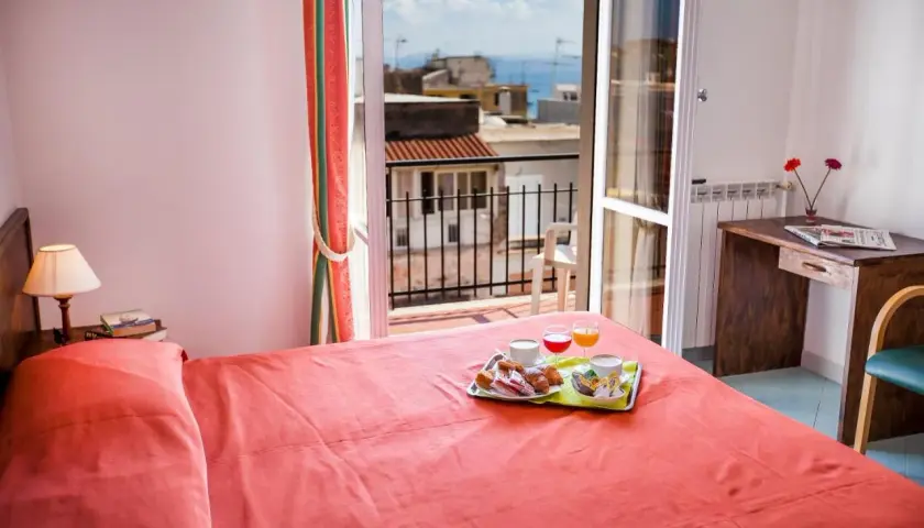 Camera con letto rosso e vassoio colazione sul letto. Vista mare dal balcone dell'hotel Conte Ischia.