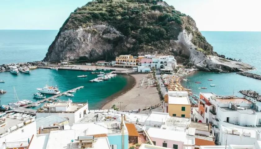 Baia con barche e case colorate a Ischia, con la rocca verde che domina il mare. Le cantine di Ischia offrono un panorama mozzafiato.