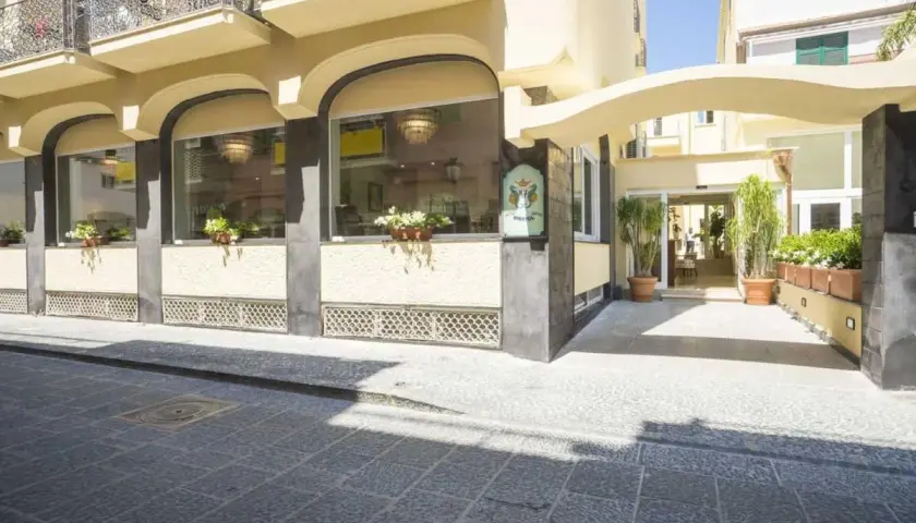 Ingresso elegante del **hotel Bristol Ischia**, con ampie vetrate, piante verdi e un'insegna storica.