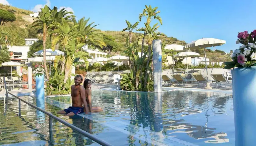 Coppia rilassata in piscina, circondata da palme e lettini, in un resort alle terme Ischia.