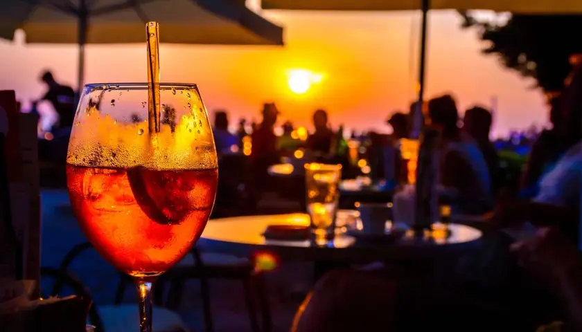 Un aperitivo rinfrescante con vista sul tramonto a Ischia centro sera. Persone sedute ai tavoli, ombrelloni e il sole che cala all'orizzonte.