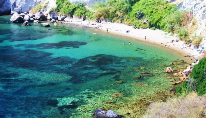 Acque cristalline e sabbia dorata nella spiaggia delle monache, incastonata tra scogliere rocciose e vegetazione rigogliosa.