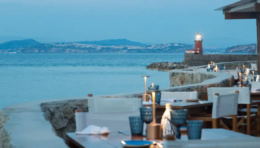 Tavoli apparecchiati con vista sul mare e un faro rosso, un invito a cena a Ischia.