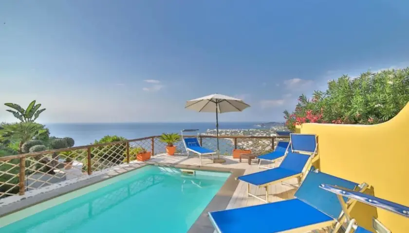 Piscina con lettini blu e vista mare a Ischia. Un angolo di paradiso, un dolce Poseidon che invita al relax.