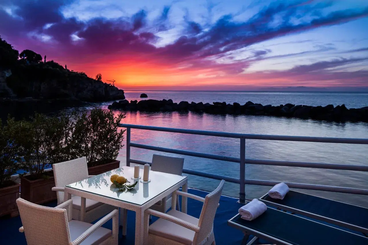 Terrazza con tavolo e sedie, lettini prendisole e un tramonto mozzafiato sul mare, un sogno in un blu resort Ischia.