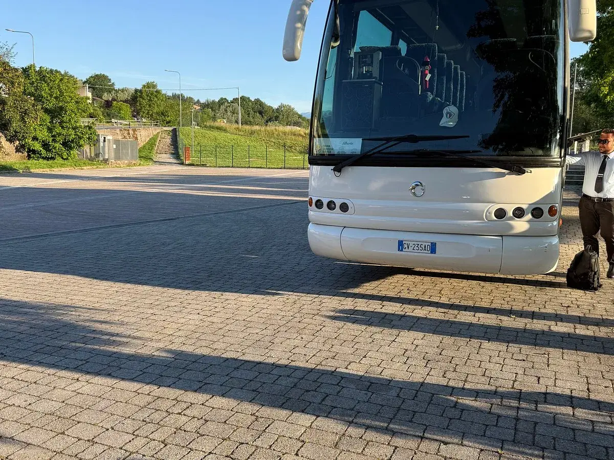 Un bus bianco attende su un parcheggio lastricato, pronto a percorrere le strade di Ischia. Un autista in divisa controlla il bagaglio.