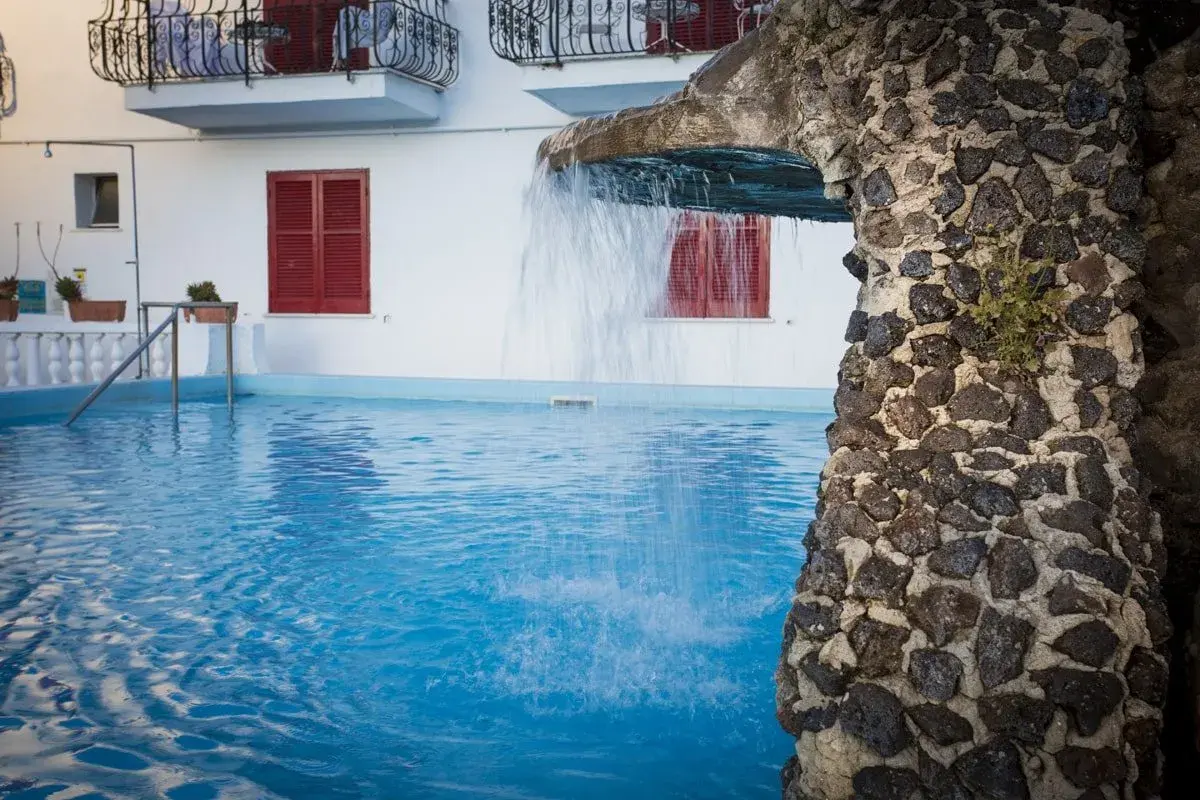 Piscina azzurra con cascata in pietra. Relax e benessere al **hotel terme Tirrenia Ischia**.