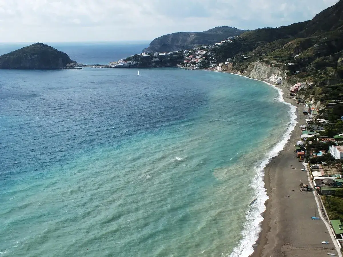 Vista aerea della spiaggia dei pescatori a Ischia, con case colorate aggrappate alla costa e un mare turchese.