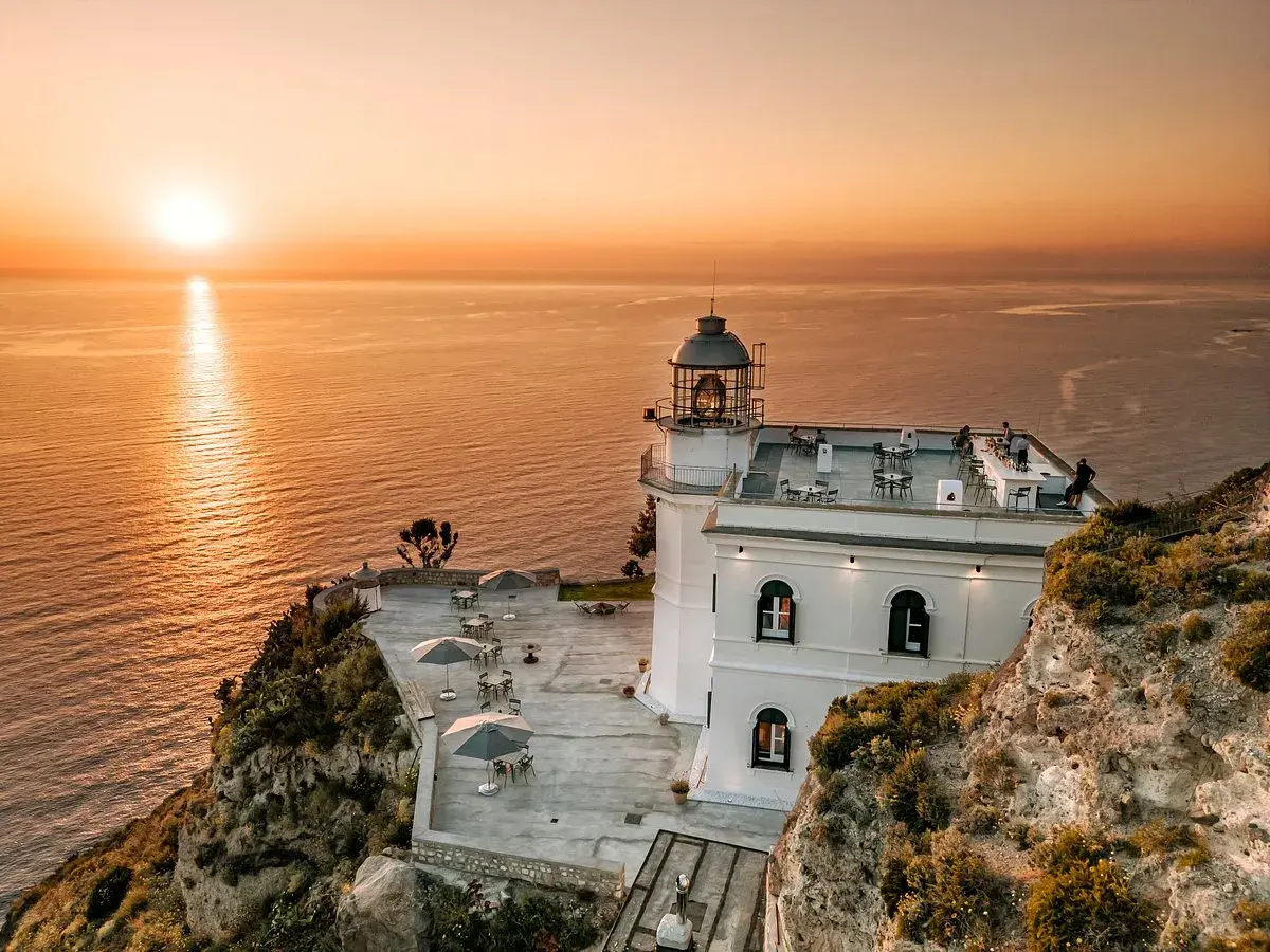 Hotel Faro Punta Imperatore a Ischia, con il sole che tramonta sul mare. Tavolini all'aperto e un bar sul tetto.