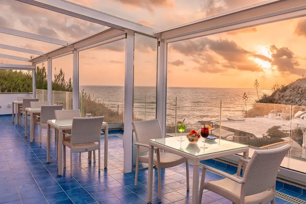 Terrazza con vista mare al tramonto, ideale per chi cerca dove alloggiare a Ischia senza macchina. Tavoli apparecchiati per aperitivo.