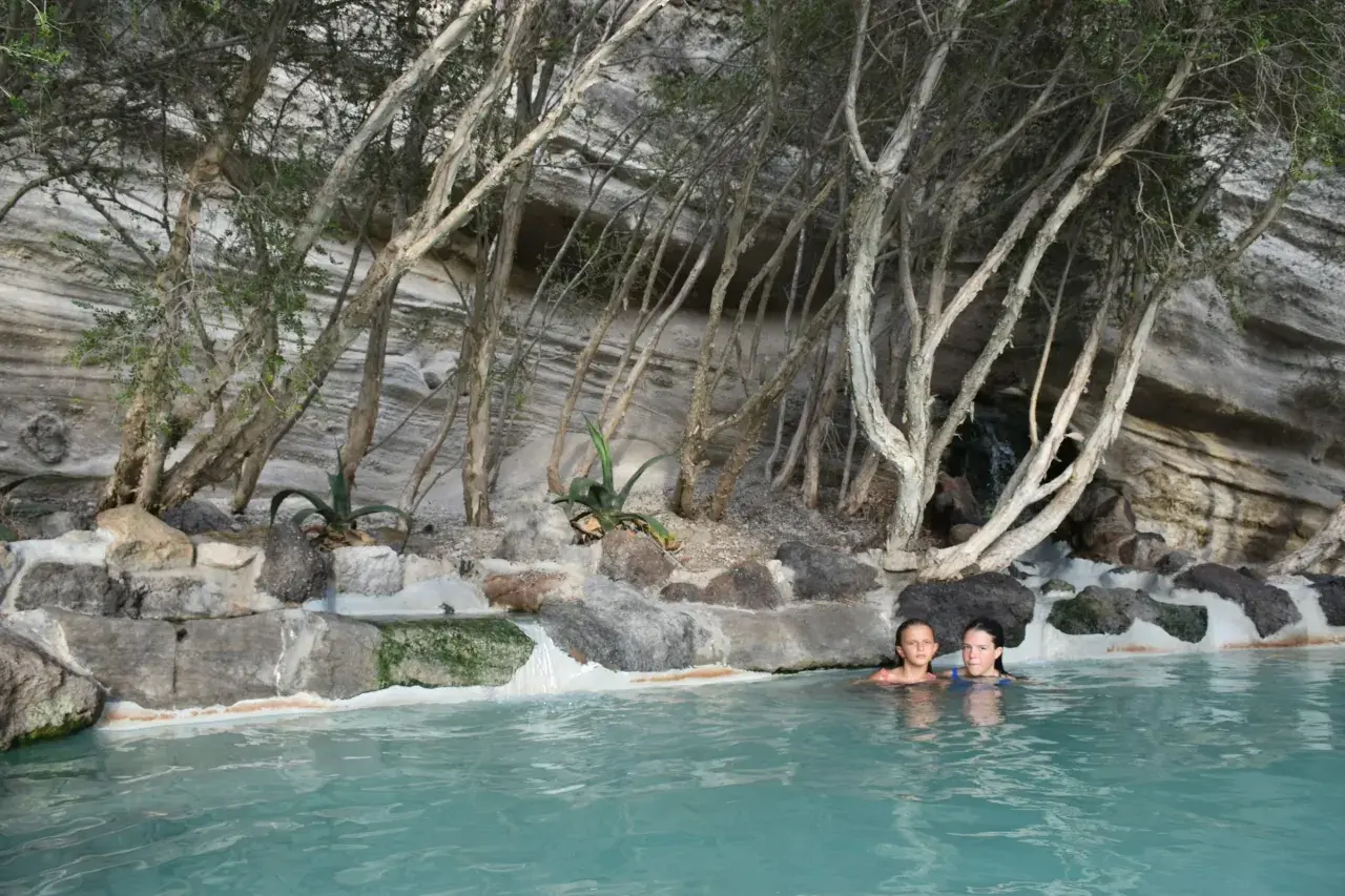 Due bambine si godono un bagno rilassante in una piscina naturale, circondata da rocce e vegetazione, un luogo perfetto per terme gratuite.