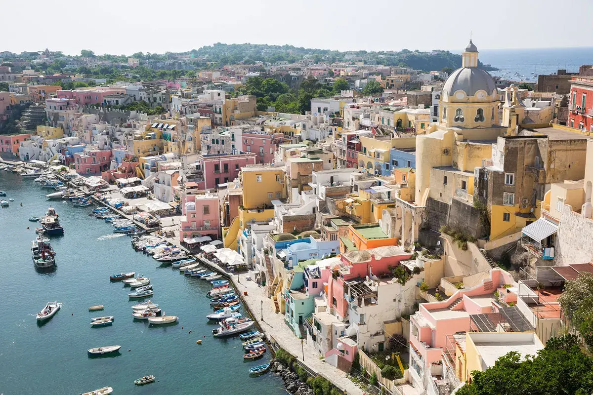 Colorate case a picco sul mare, un porto con barche. La vista ricorda la vicinanza tra Ischia e Capri, un sogno di vacanza.