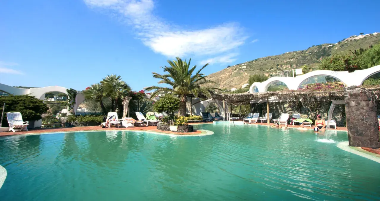 Piscina con palme e lettini, un angolo di paradiso tropicale a Ischia, con persone che si rilassano nell'acqua cristallina.
