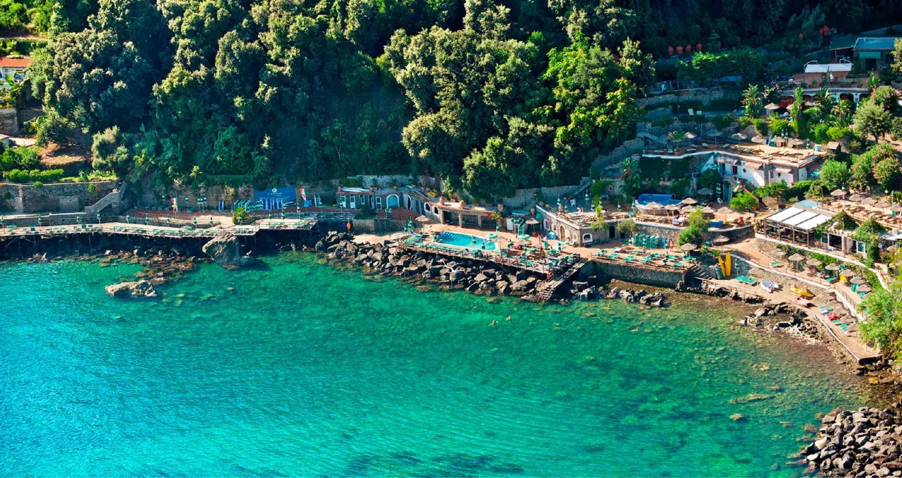 Un incantevole **bagnitiello a Ischia**, con acque cristalline, una piscina panoramica e una lussureggiante vegetazione che abbraccia la costa rocciosa.