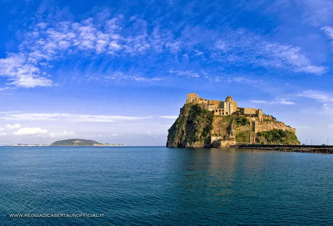 Il **palazzo reale** di Ischia, arroccato su uno scoglio, domina il mare blu sotto un cielo terso.