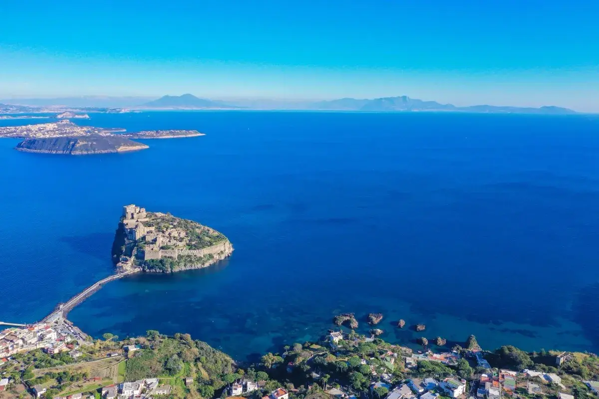 Aerial view of Castello Aragonese on a rocky island connected by a causeway to the coast of Ischia, Italy.