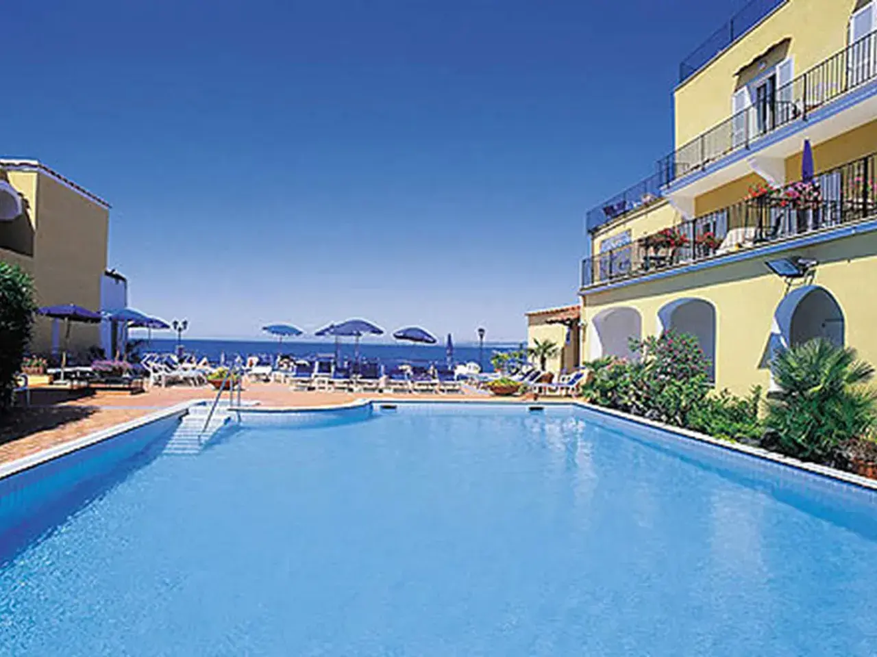 Piscina e mare azzurri al **hotel Parco Aurora Terme Ischia**. Lettini e ombrelloni invitano al relax.