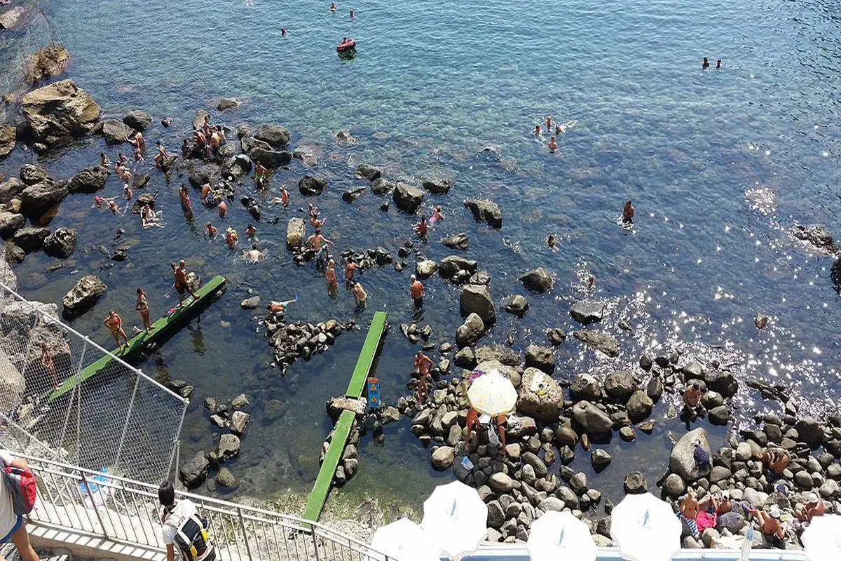 Persone si godono il sole e l'acqua cristallina nelle piscine naturali di Ischia, tra scogli e fondali trasparenti.