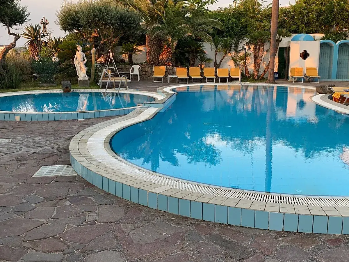 Piscine azzurre e lettini gialli al **hotel Monte Tabor**, un'oasi di relax tra palme e statue.