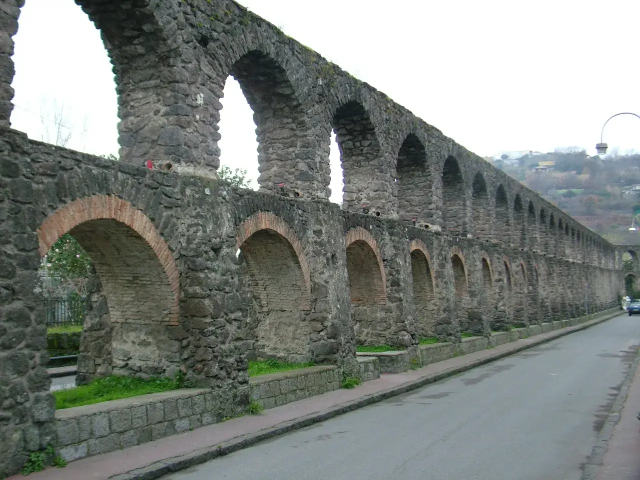 Antichi pilastri in pietra e mattoni, parte di un acquedotto a Ischia, si estendono lungo una strada.