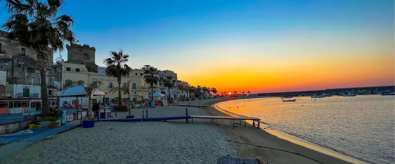 Tramonto dorato sul lungomare di Forio, Ischia. Palme, edifici storici e barche nel porto creano uno scenario incantevole.
