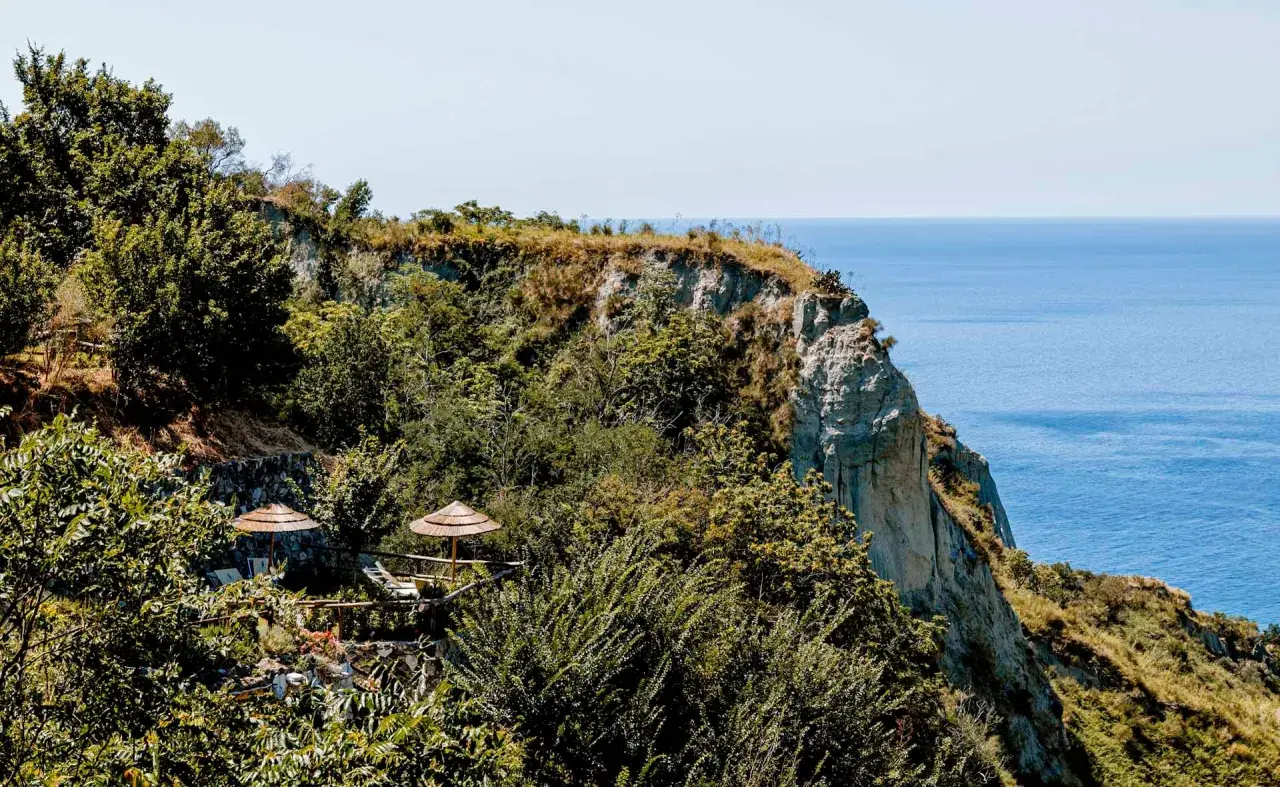 Terrazza panoramica con ombrelloni di paglia e vista sul mare a Nitrodi, Ischia.