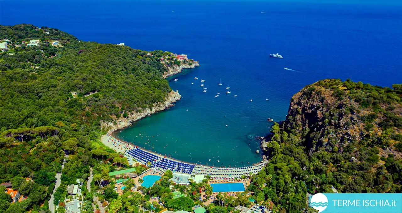 Vista aerea di una baia con spiaggia, mare blu e le piscine Negombo immerse nel verde.