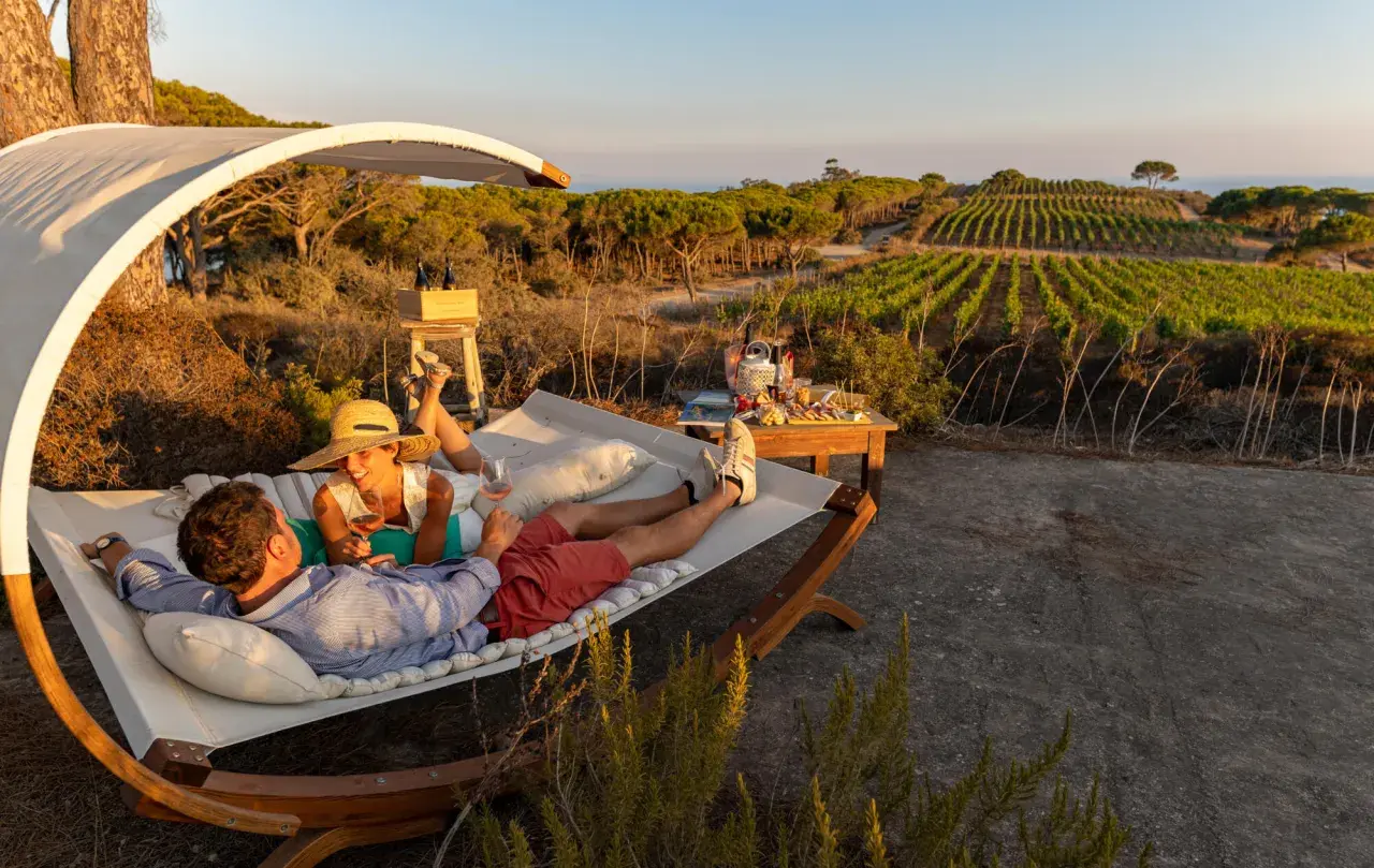 Coppia rilassata su un'amaca con vista su vigneti e mare, sorseggiando vino. Un perfetto sorgeto Ischia aperitivo al tramonto.